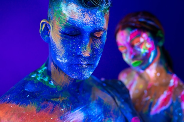 Portrait of a beefy man and woman painted in ultraviolet\
powder. body art glowing in ultraviolet light