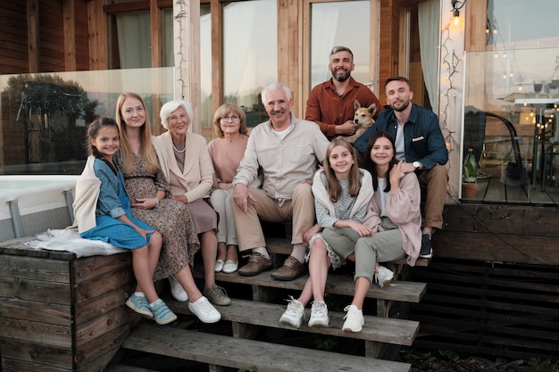 Portrait of big happy family sitting on the porch and smiling\
they gathered in their big house in the country