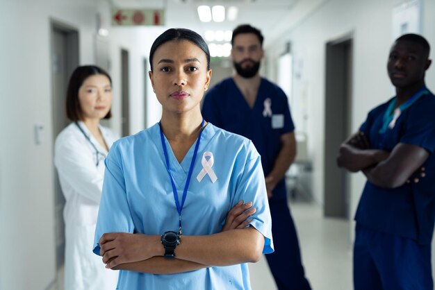 Photo portrait of biracial female healthcare worker with cancer ribbon in busy hospital corridor