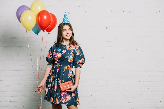 Photo portrait of a birthday girl holding balloons and gift box looking away