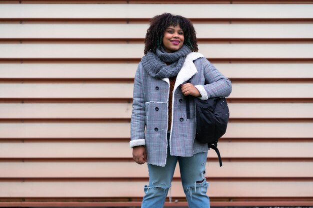 Portrait of black ethnic girl a gray wall in the university with mochica from school on the back to school