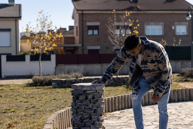 Ritratto di un uomo latino nero in occhiali da sole chinarsi per bere acqua da una fontana del parco in estate