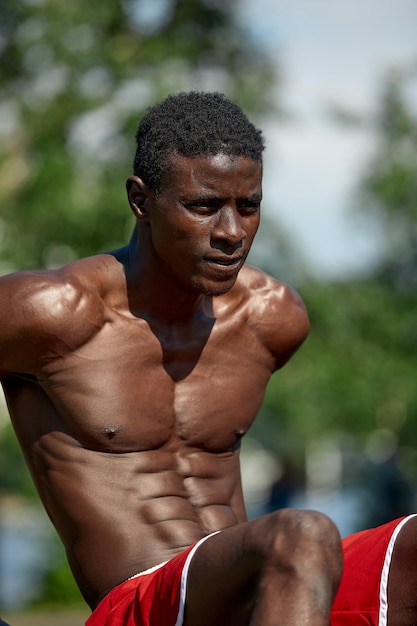 Портрет темнокожего мужчины, тренирующегося на открытом воздухе в парке. Он использует тренажер для грудной клетки.