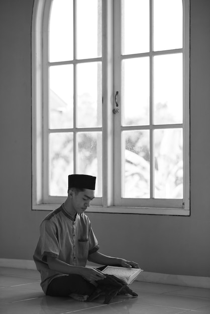 Foto immagine in bianco e nero del ritratto di giovane uomo musulmano asiatico che legge il corano santo su ramadan kareem alla moschea