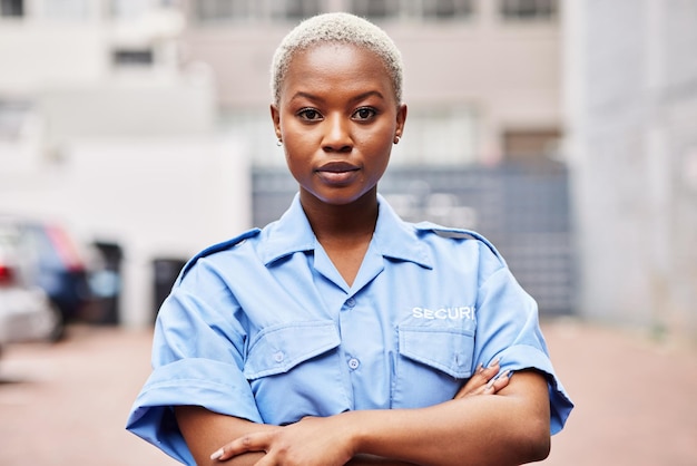 Portrait black woman and security guard with arms crossed for surveillance service safety and urban watch Law enforcement bodyguard or serious female police officer in blue shirt for city patrol