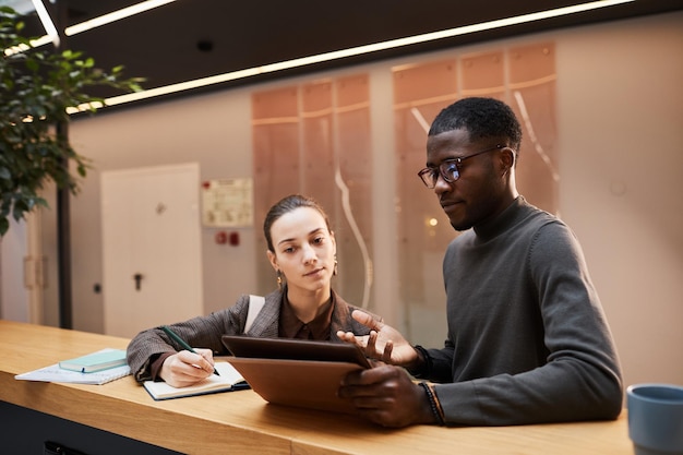 Portrait of black young businessman talking to female colleague while discussing workin hall at mode