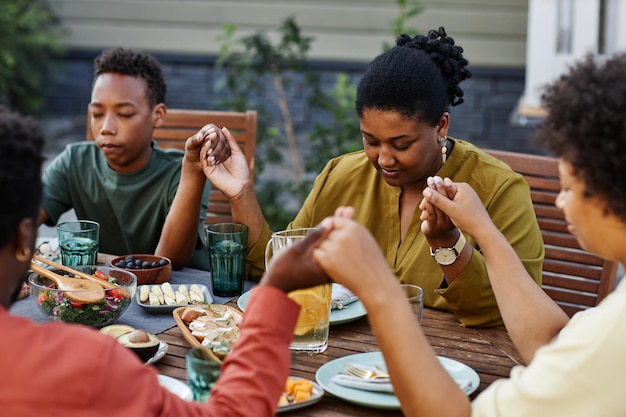 Photo portrait of black young woman saying grace at table outdoors during family gathering and holding han