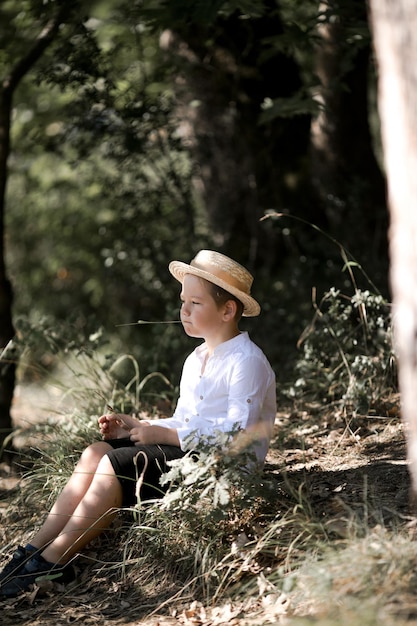 ぼやけた夏の緑の背景を持つ麦わら帽子の金髪の髪の少年の肖像画