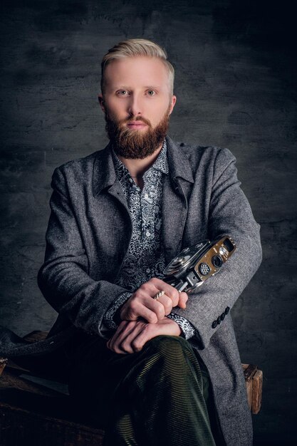 Portrait of a blond bearded male holds old vintage 8mm video camera.