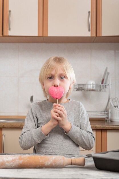 Portrait of blond boy in kitchen with pink lollipop in his hands