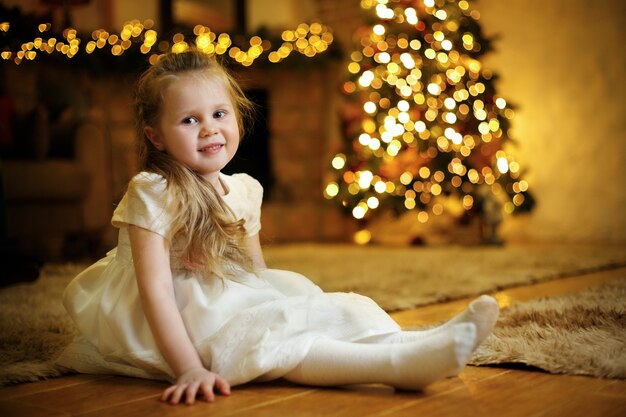クリスマスツリーを背景に3-5歳の金髪のかわいい女の子の肖像画
