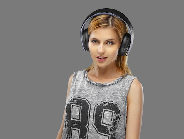 Portrait of blond female in earphones isolated on grey background.