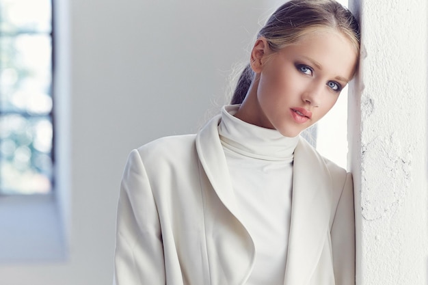 Photo portrait of blond female with blue eyes and in white clothes.