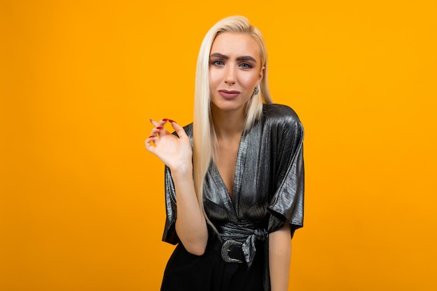 Portrait of blond lady pointing finger to wall on yellow wall