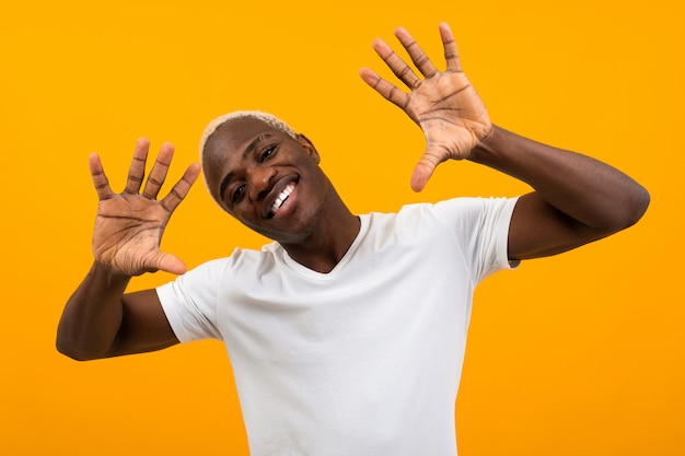 Portrait of a blond smiling charismatic african black man stalking hands to the sides in a white t-shirt on an orange studio background