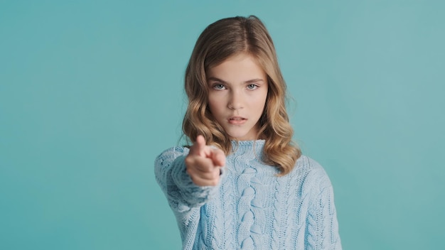 Портрет блондинки-подростка, выглядящей серьезно, показывающей указательный палец в камеру на красочном фоне