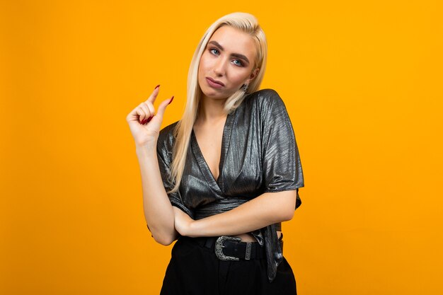 Portrait of a blonde attractive displeased young woman with holding hands on orange studio