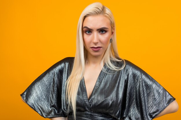 Portrait of a blonde attractive displeased young woman on yellow studio background