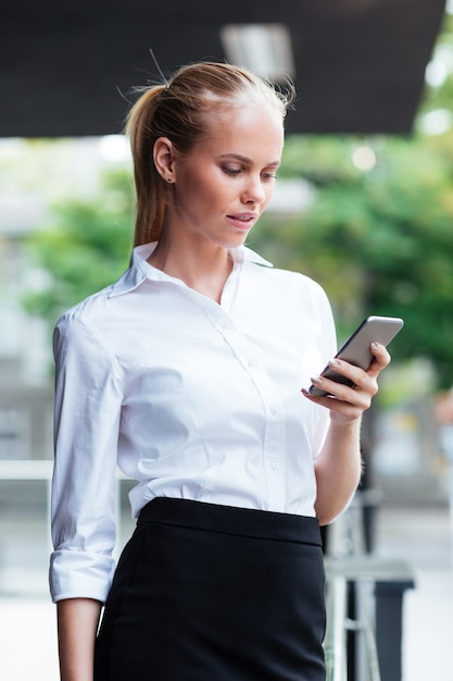 Portrait of a blonde businesswoman texting message while standing outdoors