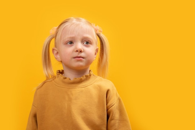 Portrait blonde caucasian female child wears yellow sweatshirt looking in the distance Bright yellow background Close up