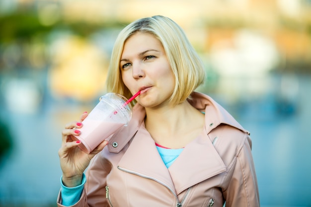 Portrait of blonde drinking milkshake in park, blurred background