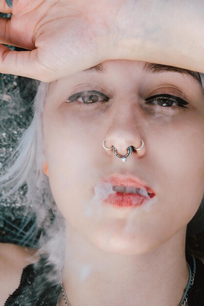 Portrait of a blonde female lying on the ground and smoking with her hand on her face