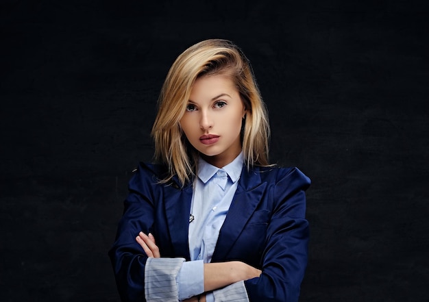 Портрет блондинки со скрещенными руками, одетой в синюю куртку.