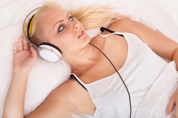 Portrait of a blonde girl lying in a bed listening to music.