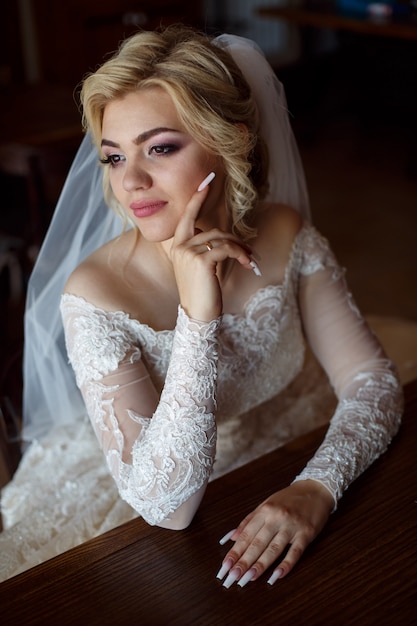 Portrait of a blonde happy bride in luxury white dress and long veil indoor close up. young smiling  bride with gentle makeup . wedding day