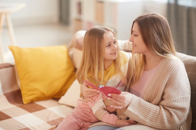 Foto ritratto di bambina bionda che abbraccia la mamma mentre celebrava la festa della mamma insieme seduti sul divano accogliente a casa, copia dello spazio