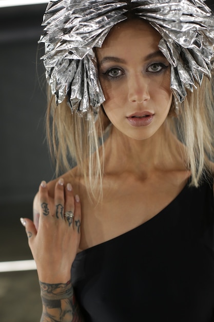 Portrait of a blonde model with bright makeup tattoos on the body and silver foil on her hair for hair dyeing modern fashion shooting high quality photo