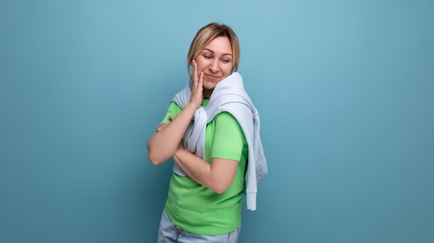 Portrait of blonde positive modest young woman in casual outfit on studio blue background with copy