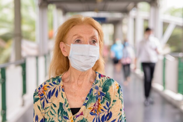 Portrait of blonde senior woman with mask thinking at the footbridge