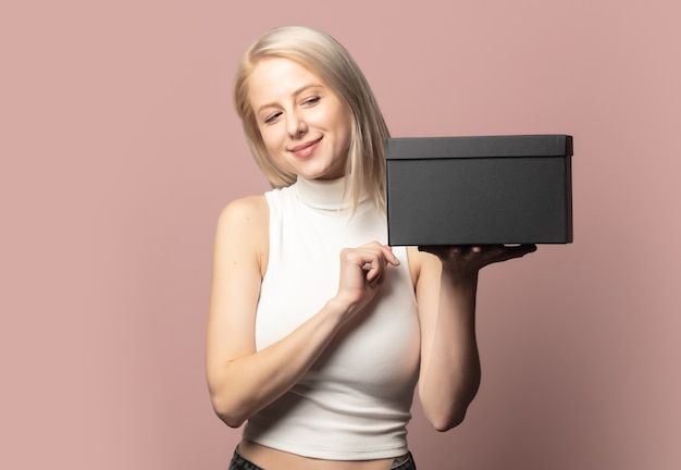 Portrait of blonde in top with black gift box on pink