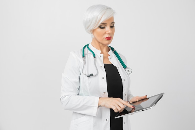 Portrait of blonde woman in doctors costume with tablet in her hands isolated   