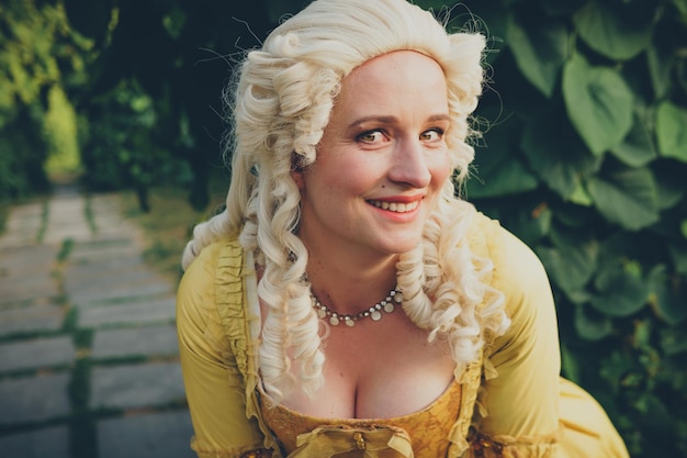 Portrait of blonde woman dressed in historical Baroque clothes with old fashion hairstyle outdoors