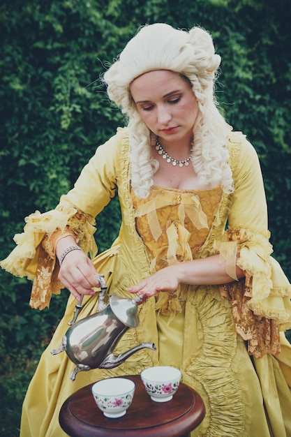 Portrait of blonde woman dressed in historical Baroque clothes with old fashion hairstyle outdoors