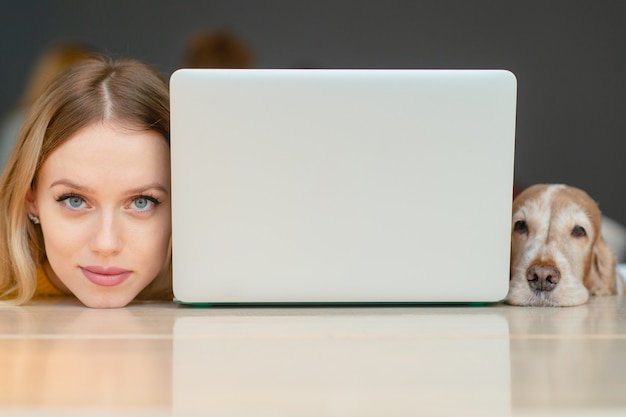 portrait of blonde woman head and head of her cocker spaniel dog lying together on a table along the edges of laptop