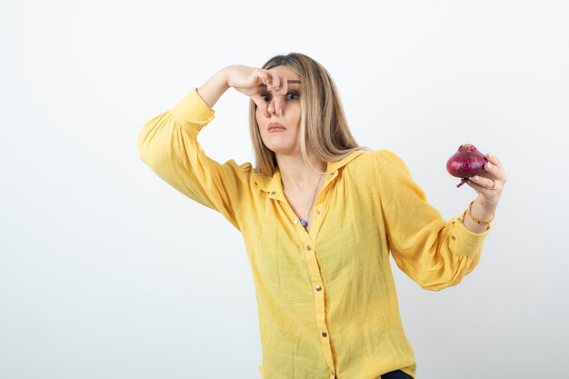 Portrait of blonde woman holding red onion with disgusted expression