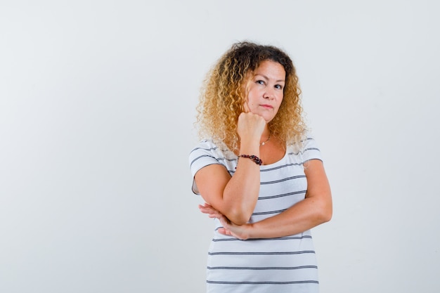 Foto ritratto di donna bionda che si appoggia il mento sul pugno alzato con una maglietta a righe e guarda una vista frontale pensierosa