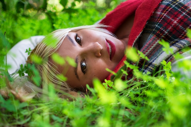 Portrait of a blonde woman lying among the forest clovers.