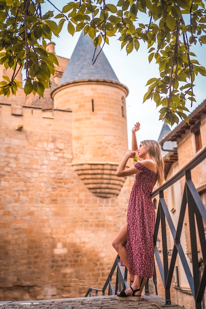 Portrait of a blonde woman next to a medieval castle in a red dress