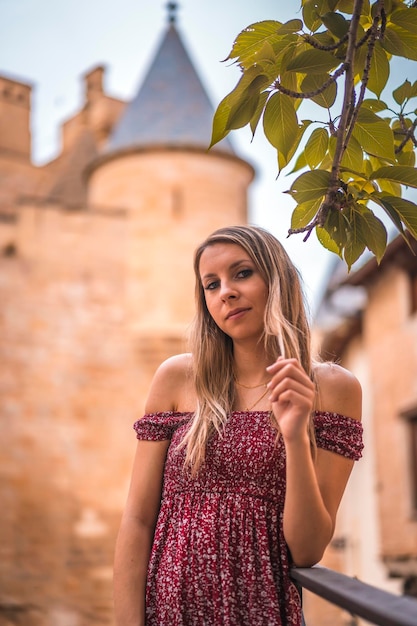 Портрет блондинки рядом со средневековым замком в красном платье
