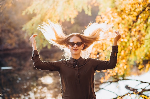 Foto ritratto di una donna bionda in occhiali da sole nella foresta di autunno