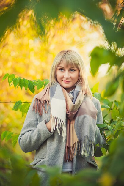 Portrait of blonde woman with a short haircut walks through the\
forest in a gray wool coat and a plaid scarf