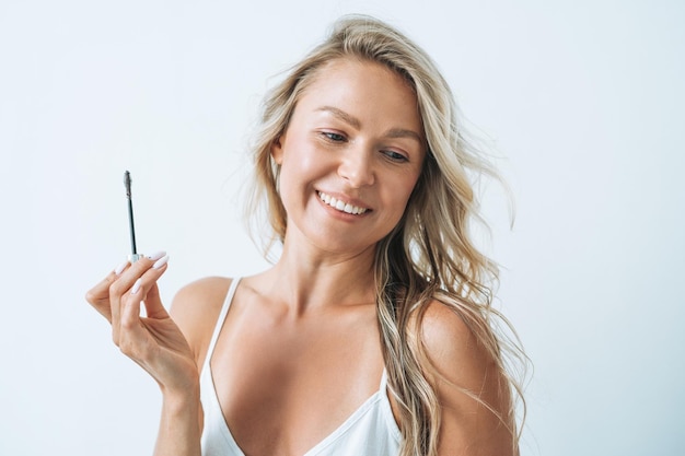 Portrait of blonde young woman with eyebrow mascara brush on white background