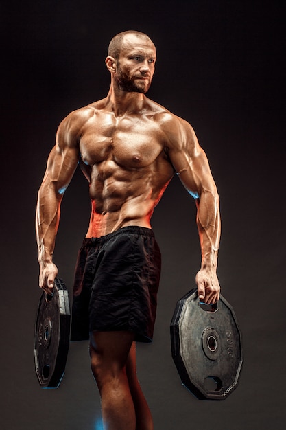 Photo portrait of bodybuilder with dumbbells in his arms on grey backg