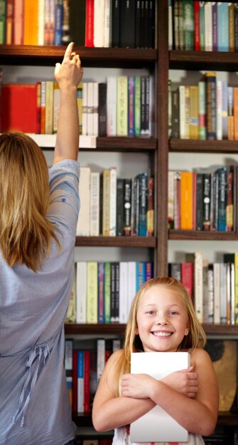 Foto ritratto di libri e bambini in biblioteca con sorriso eccitato apprendimento e rilassamento con conoscenza di studio racconto di storie di mamma e figlia felici in libreria insieme a fantasie di storie e istruzione nella lettura