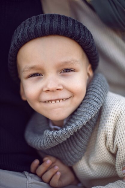 Portrait of a boy child in autumn in a knitted hat sitting with his parents in a field