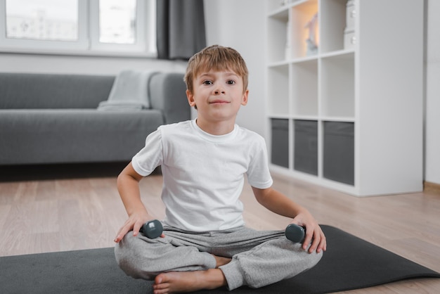 portrait of boy child exercising with dumbbells at home boy sitting on a sports mat